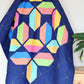 Flourishing quilt pattern in scrappy colours pink, peach, yellow, blue, green and lime on a navy blue background on a quilt ladder
