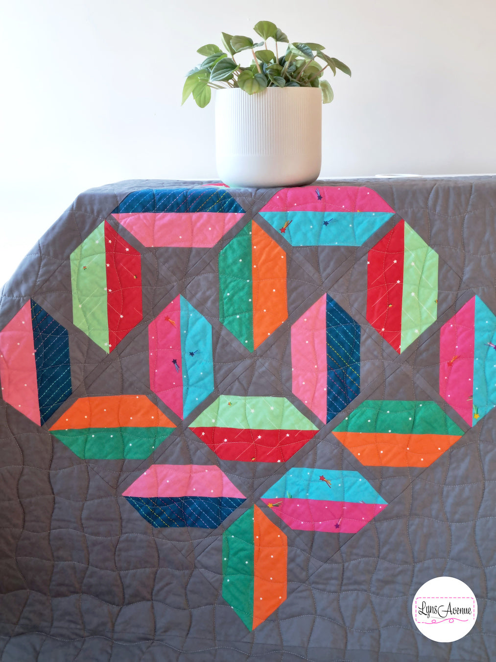 Flourishing quilt in scrappy colours, red, blue, orange, green and pink on a grey background