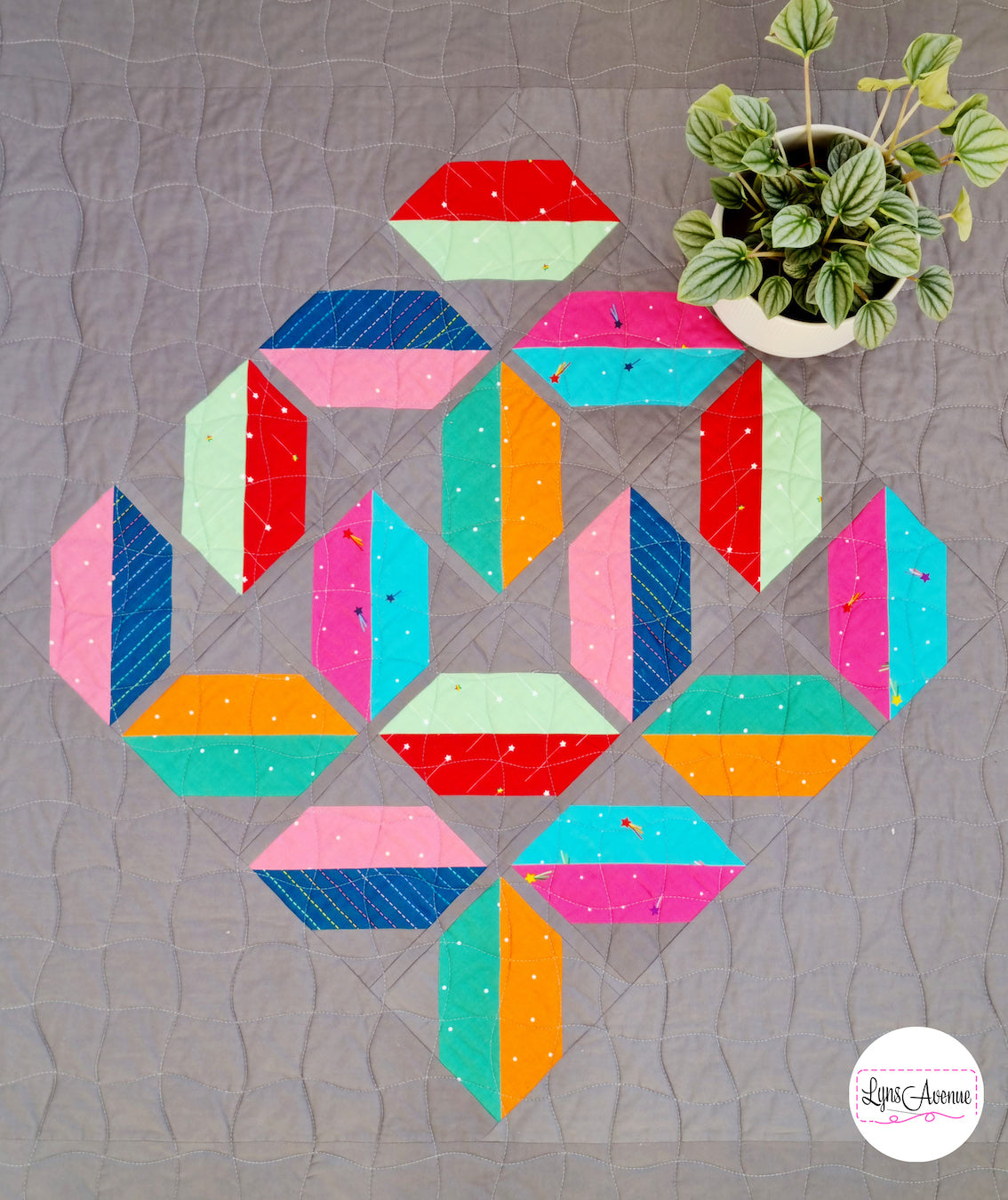 Flourishing quilt in scrappy colours, red, blue, orange, green and pink on a grey background