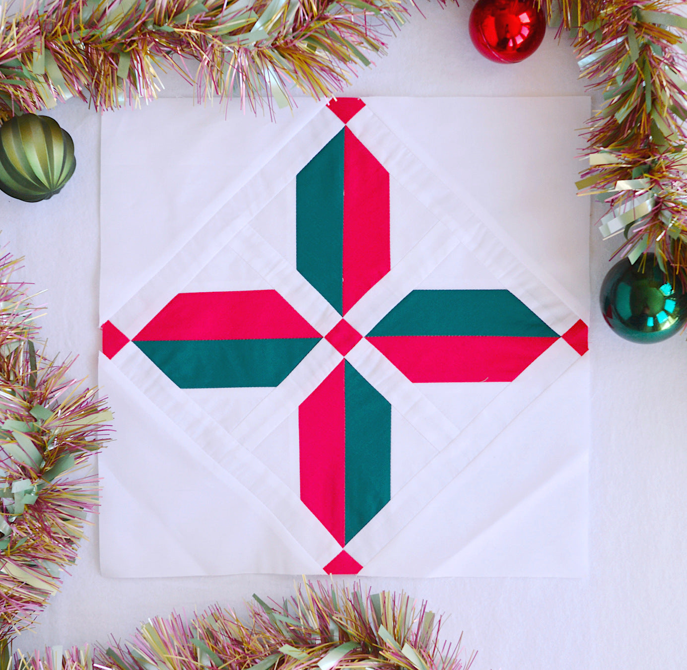 Shown here is a star quilt block in red and green colours surrounded by red and green baubles and tinsel