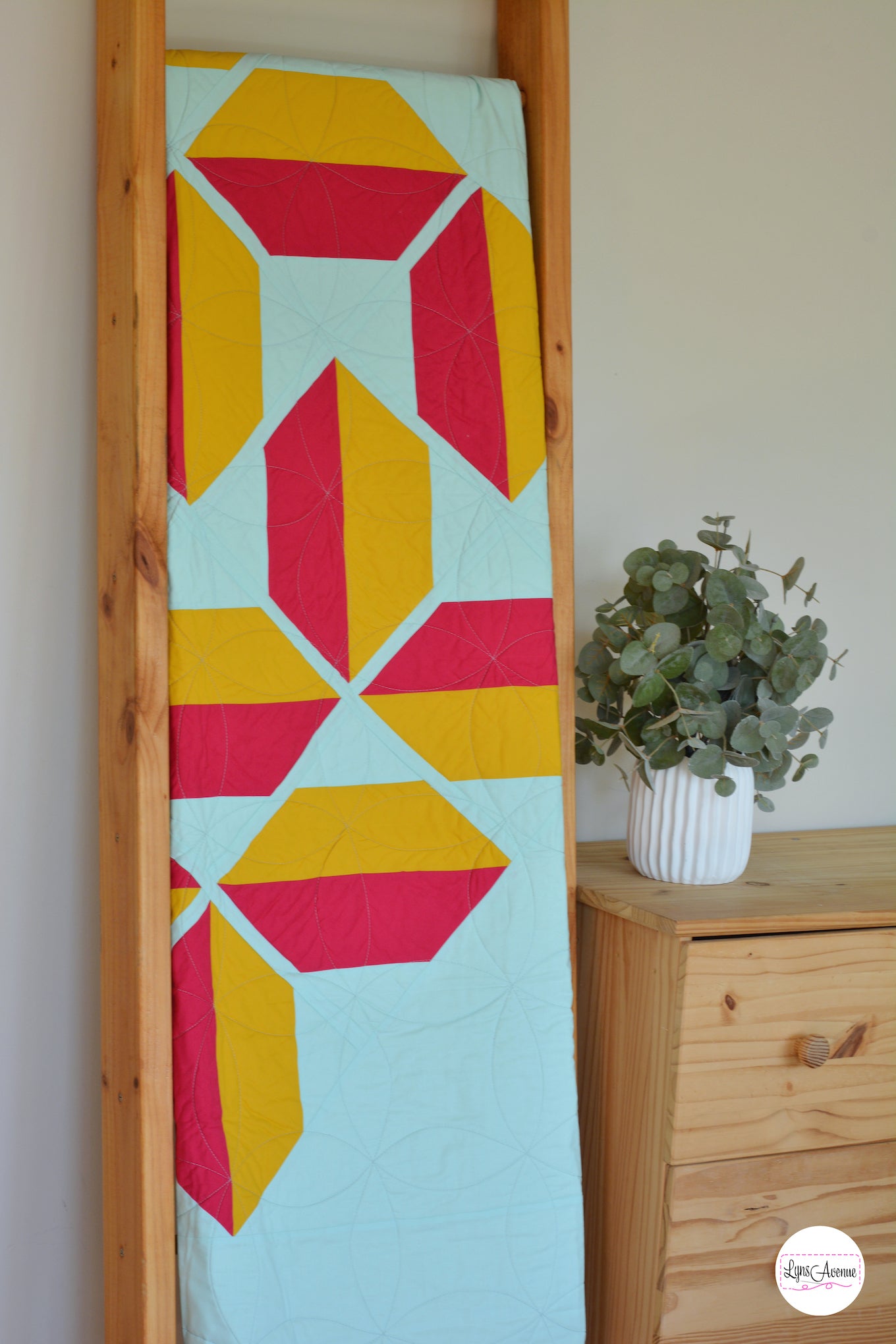 Flourishing quilt in two colour version of red and yellow on a light green background on a quilt ladder
