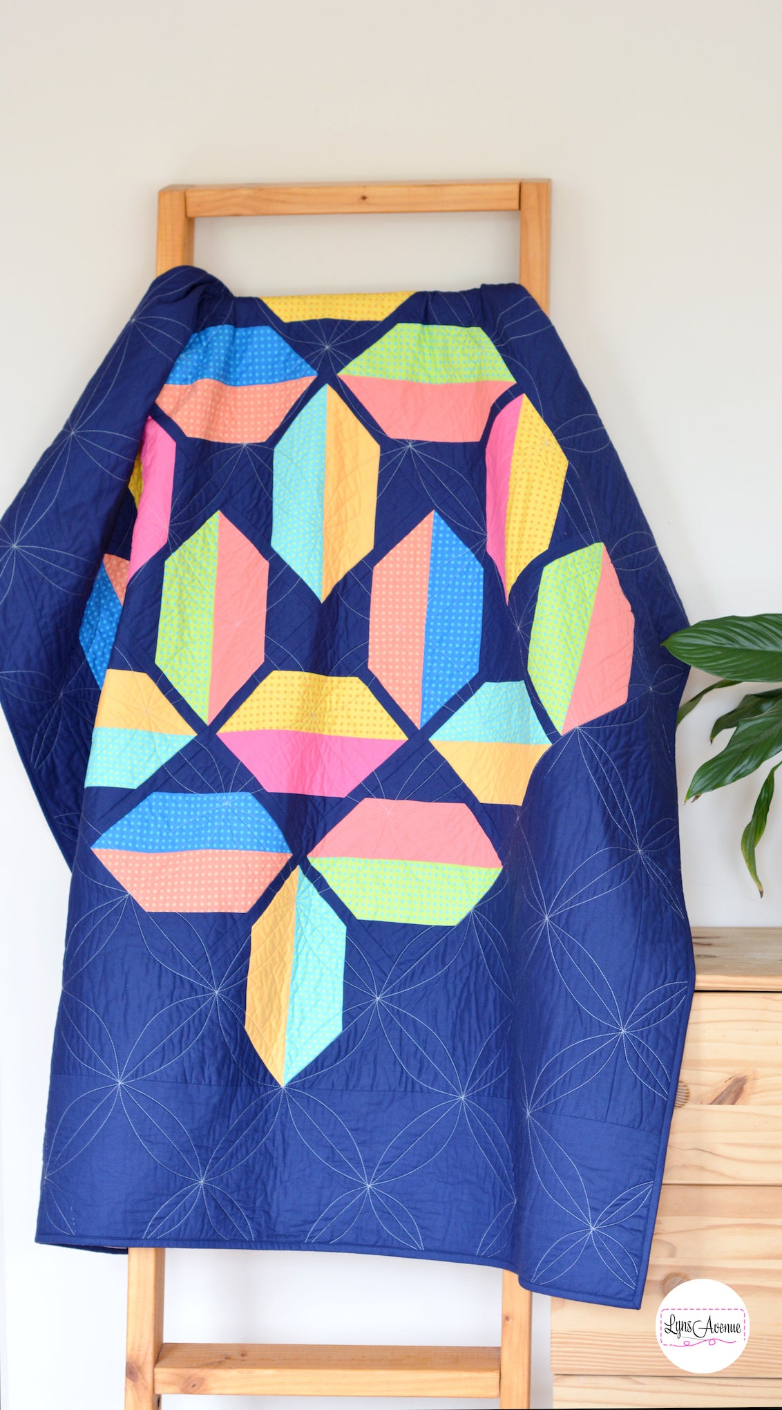 Flourishing quilt pattern in scrappy colours pink, peach, yellow, blue, green and lime on a navy blue background on a quilt ladder