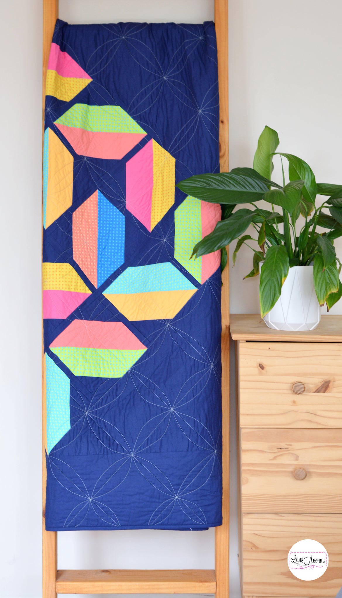 Flourishing quilt pattern in scrappy colours pink, peach, yellow, blue, green and lime on a navy blue background on a quilt ladder