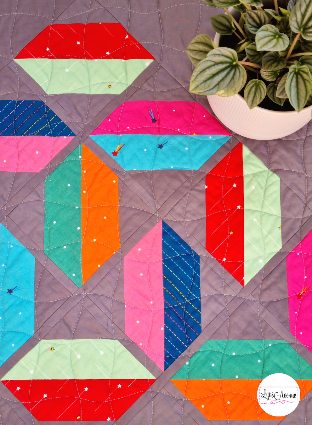 Flourishing quilt in scrappy colours, red, blue, orange, green and pink on a grey background